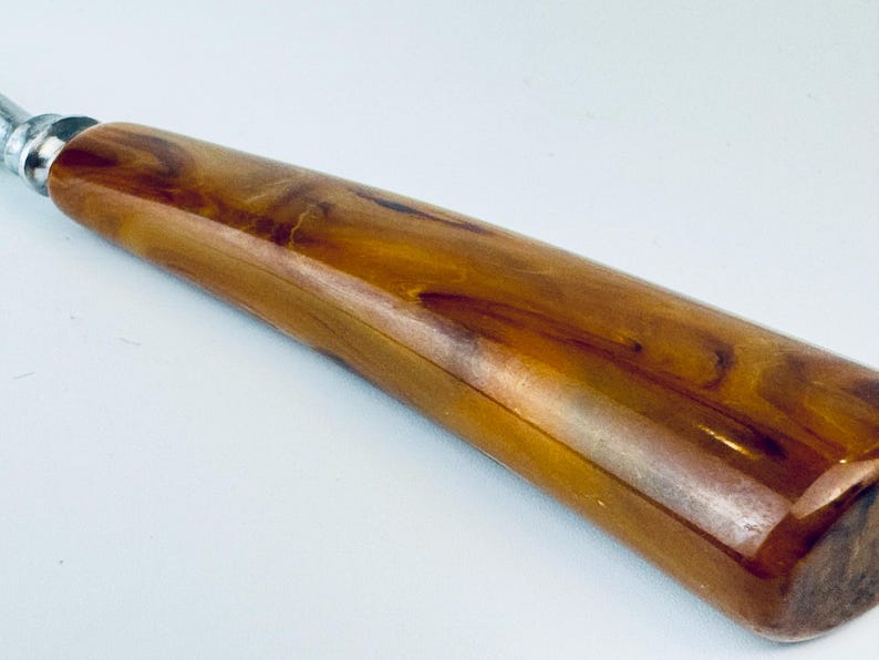 May include: A close-up of a brown and gold bottle opener with a long, smooth handle. The handle is made of a marbled plastic material.