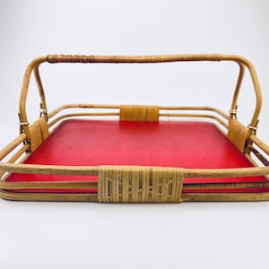 Op de afbeelding: Een vierkant rieten dienblad met een rode voering en een handvat. Het dienblad is gemaakt van natuurlijk geweven riet en heeft een glad rood oppervlak aan de binnenkant.