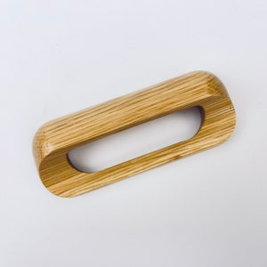 May include: A wooden drawer pull with a rectangular shape and a cutout in the centre. The pull is made of light brown wood with visible grain.