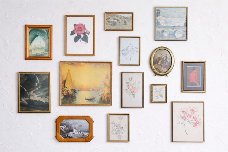 May include: A collection of framed art pieces, including landscape paintings, floral prints, and architectural sketches, arranged on a white wall. The frames vary in shape and size, with gold and wood finishes.