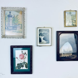 May include: A collection of framed art pieces, including a landscape painting of a fountain, a botanical print of a rose, and a vintage photograph of a waterfall. The frames vary in style, from ornate gold to dark wood.