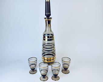 May include: A set of clear glass decanter and shot glasses with gold and black stripes. The decanter has a black stopper.
