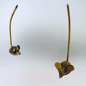 Peut inclure: Deux figurines de souris en métal couleur or avec de longues queues. Les souris sont tournées dans des directions différentes.