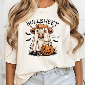 May include: A cream-coloured t-shirt with a Halloween graphic. The design shows a cow in a ghost costume, a jack-o'-lantern, and the text "BULLSHEET" above, with "moo... I mean boo" below. Black bats are also included in the design.