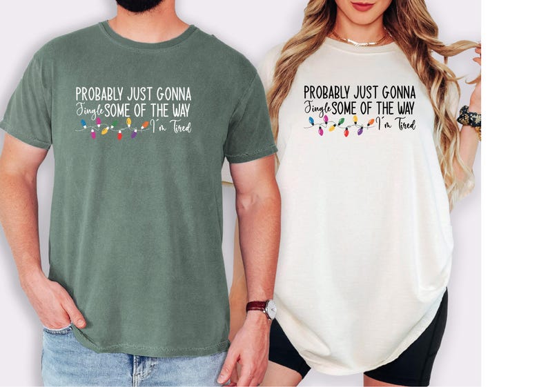 Puede incluir: Dos camisetas, una verde salvia y otra blanquecina, cada una con el texto "PROBABLY JUST GONNA Jingle SOME OF THE WAY I'm Tired" y una cadena de luces navide&ntilde;as de colores. Las camisetas son de manga corta.