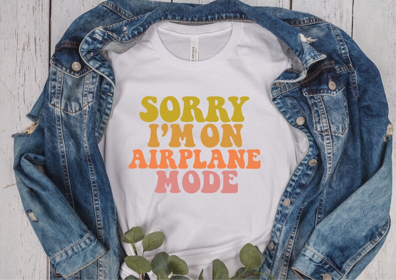 May include: White t-shirt with the text "Sorry I'm on Airplane Mode" in a retro font with yellow, orange, and pink colors.