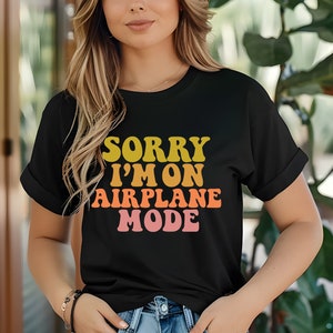 May include: A black t-shirt with the text "SORRY I'M ON AIRPLANE MODE" in a retro font with yellow, orange, and pink colors.