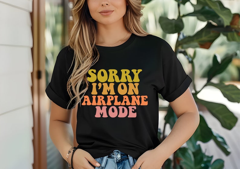 May include: A black t-shirt with the text "SORRY I'M ON AIRPLANE MODE" in a retro font with yellow, orange, and pink colors.