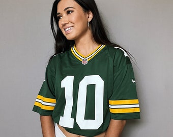 May include: A woman wearing a green and white jersey with the number 10 on the front. The jersey has yellow and white stripes on the sleeves. She is wearing white shorts and has long dark hair.