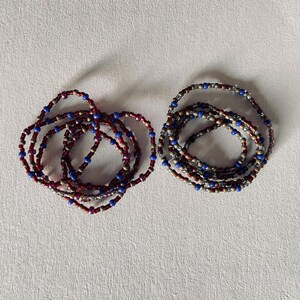 Puede incluir: Dos pulseras de cuentas, una en tonos rojos, dorados y azules, y la otra en tonos grises, dorados y azules.