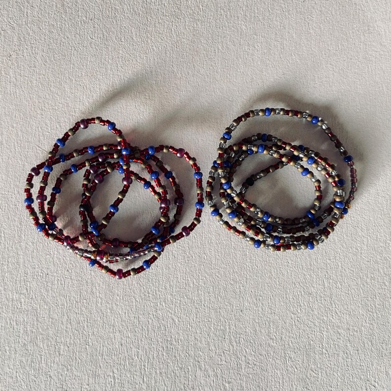 Puede incluir: Dos pulseras de cuentas, una en tonos rojos, dorados y azules, y la otra en tonos grises, dorados y azules.