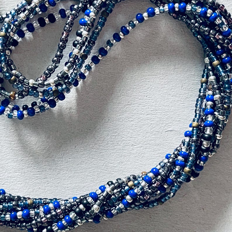 May include: A multi-strand beaded necklace with blue, silver, and gold beads. The necklace is made of small, round beads and is arranged in a circular pattern.