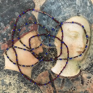 Puede incluir: Primer plano de un collar de cuentas con cuentas marrones, azules y plateadas. El collar est&aacute; sobre una superficie texturizada con un dise&ntilde;o pintado.