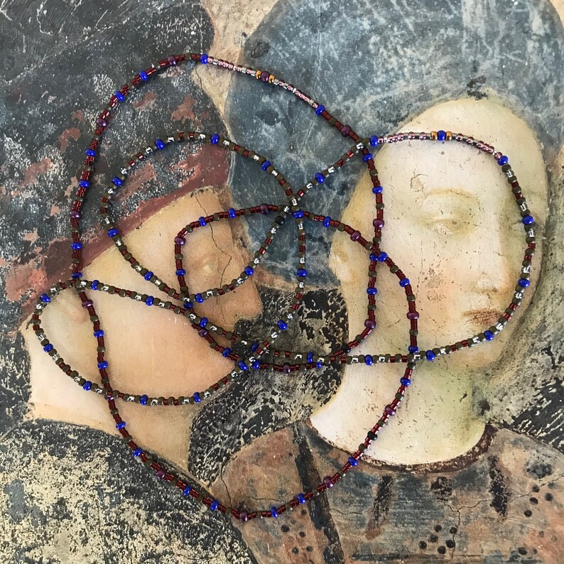Puede incluir: Primer plano de un collar de cuentas con cuentas marrones, azules y plateadas. El collar est&aacute; sobre una superficie texturizada con un dise&ntilde;o pintado.