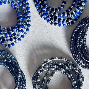 May include: A collection of beaded bracelets in shades of blue, black, and silver. The bracelets are made of small, round beads and are arranged in a circular pattern.