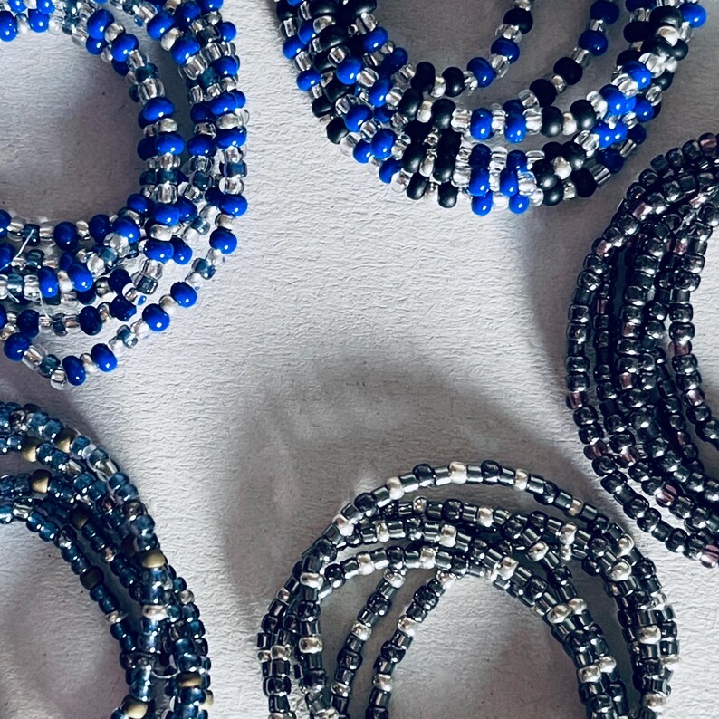 May include: A collection of beaded bracelets in shades of blue, black, and silver. The bracelets are made of small, round beads and are arranged in a circular pattern.