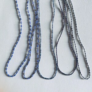 May include: Five strands of beaded necklaces in shades of blue and silver. The necklaces are made of small, round beads and are arranged in a parallel pattern.