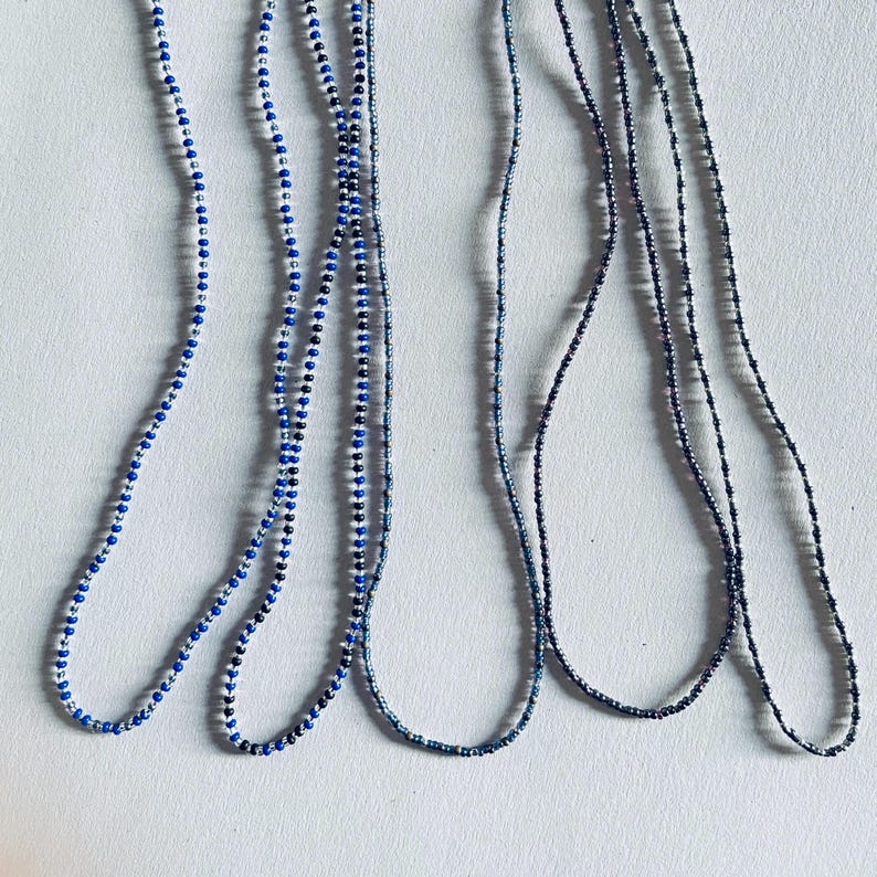 May include: Five strands of beaded necklaces in shades of blue and silver. The necklaces are made of small, round beads and are arranged in a parallel pattern.