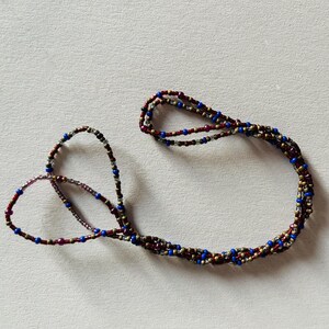 Puede incluir: Un collar de cuentas de m&uacute;ltiples hilos con cuentas rojas, azules y doradas.
