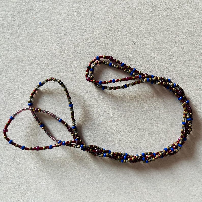 Puede incluir: Un collar de cuentas de m&uacute;ltiples hilos con cuentas rojas, azules y doradas.