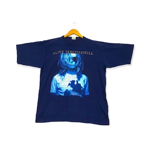 Può includere: Una maglietta blu navy con un'immagine blu sbiadita di una persona con occhiali da sole e il testo "ALIVE JEHOVAHKILL" stampato sul davanti.