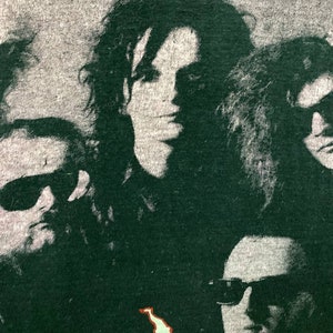Puede incluir: Una camiseta vintage de banda en blanco y negro con una foto de cuatro personas con gafas de sol. Los miembros de la banda est&aacute;n en verde oscuro y el fondo es gris claro.