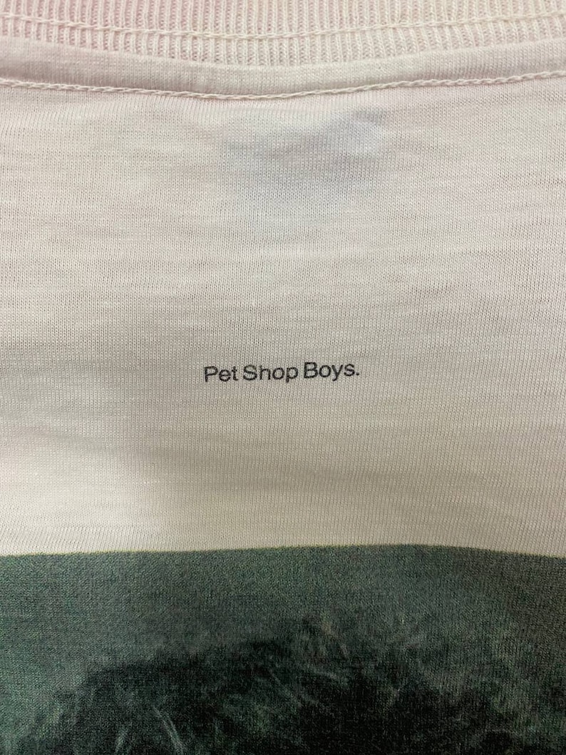 Puede incluir: Primer plano de una camiseta blanca con el texto "Pet Shop Boys." impreso en negro.