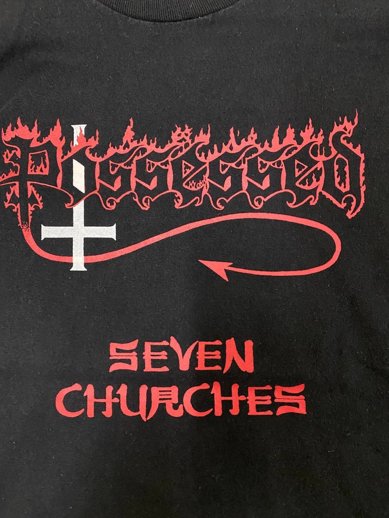 May include: Black t-shirt with a red and white graphic of the word "Possessed" in a stylized font with flames and a cross. The text "Seven Churches" is printed below the graphic.