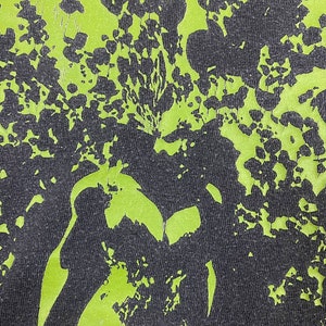 May include: A black and green fabric with a distressed, faded, and cracked green print. The print is a pattern of abstract shapes and lines.