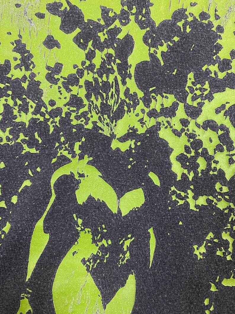 May include: A black and green fabric with a distressed, faded, and cracked green print. The print is a pattern of abstract shapes and lines.