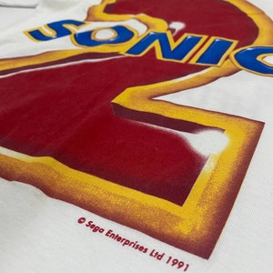 May include: White t-shirt with a red and yellow graphic of the number "2" with the word "SONIC" in blue letters above it. The text "&copy; Sega Enterprises Ltd 1991" is printed below the graphic.