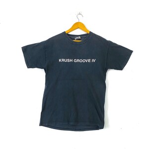 K&ouml;nnte beinhalten: Ein schwarzes T-Shirt mit dem Aufdruck "KRUSH GROOVE IV" in wei&szlig; auf der Vorderseite.