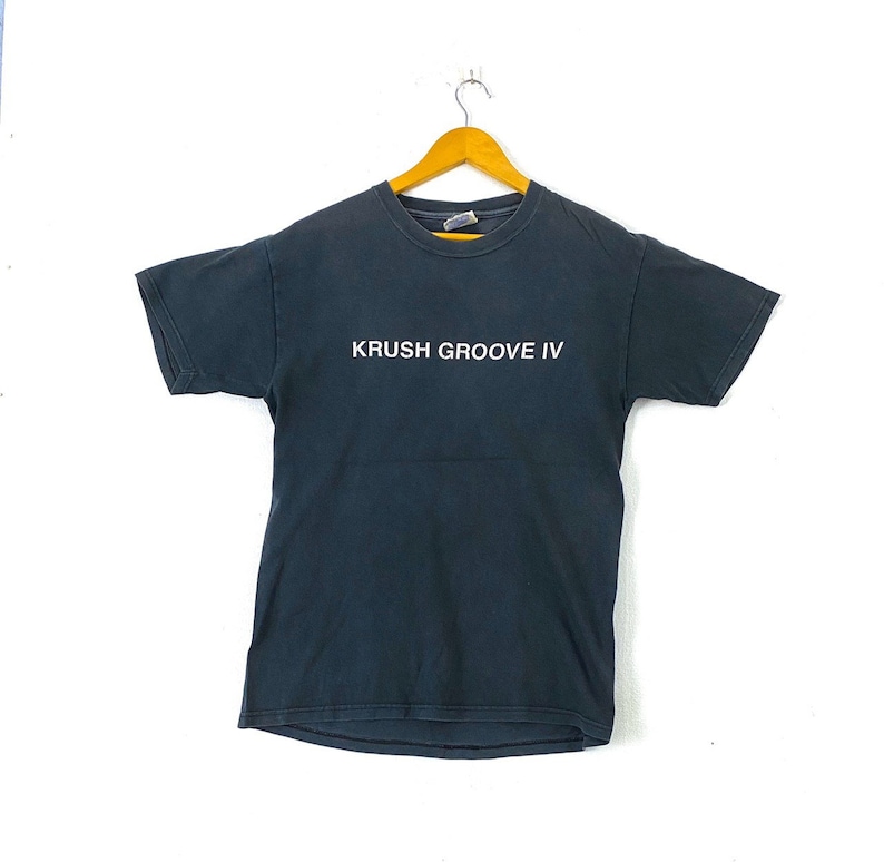 K&ouml;nnte beinhalten: Ein schwarzes T-Shirt mit dem Aufdruck "KRUSH GROOVE IV" in wei&szlig; auf der Vorderseite.