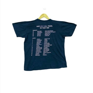 Puede incluir: Una camiseta negra con texto blanco que enumera las fechas y ubicaciones de una gira del Reino Unido de 1989 para la banda "Have Love Will Travel".