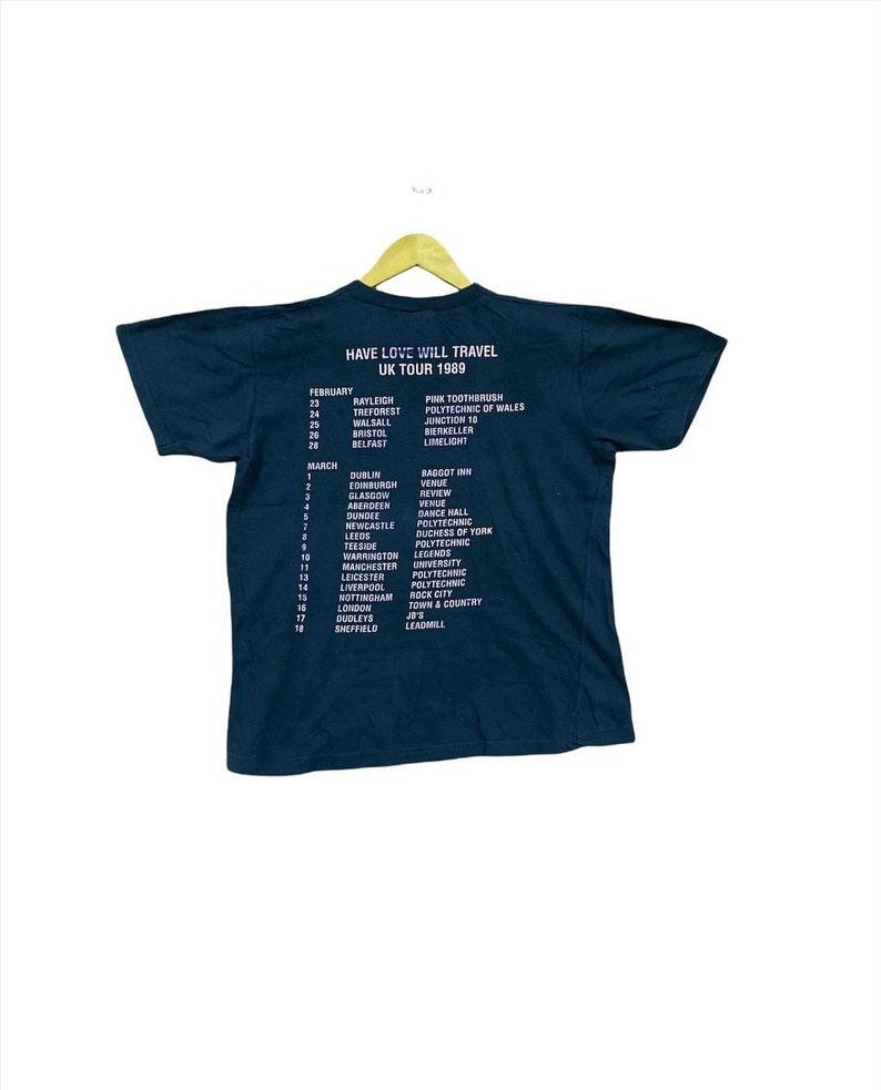 Puede incluir: Una camiseta negra con texto blanco que enumera las fechas y ubicaciones de una gira del Reino Unido de 1989 para la banda "Have Love Will Travel".