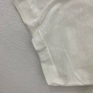 May include: Close-up of the white cotton fabric of a t-shirt, showing the stitching detail of the sleeve seam.