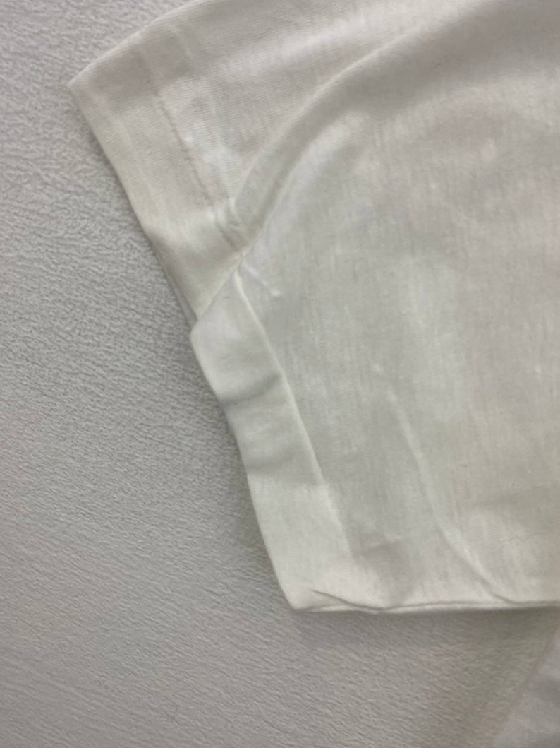 May include: Close-up of the white cotton fabric of a t-shirt, showing the stitching detail of the sleeve seam.