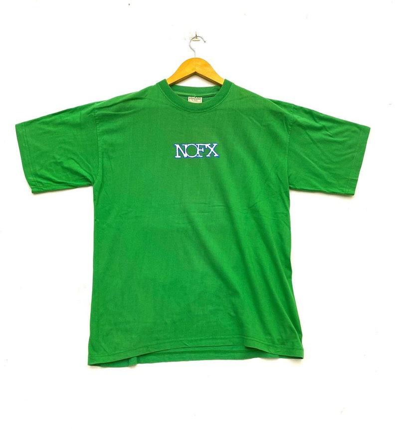 Puede incluir: Camiseta verde de manga corta con un logotipo "NOFX" azul y blanco en la parte delantera.