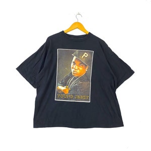 May include: Black t-shirt with a graphic print of rapper Young Jeezy wearing a black and gold baseball cap. The text "YOUNG JEEZY" is printed below the image.