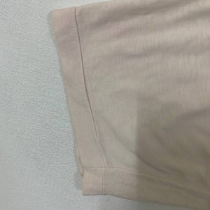 Puede incluir: Primer plano del dobladillo de una camiseta rosa claro. El dobladillo est&aacute; doblado y cosido.