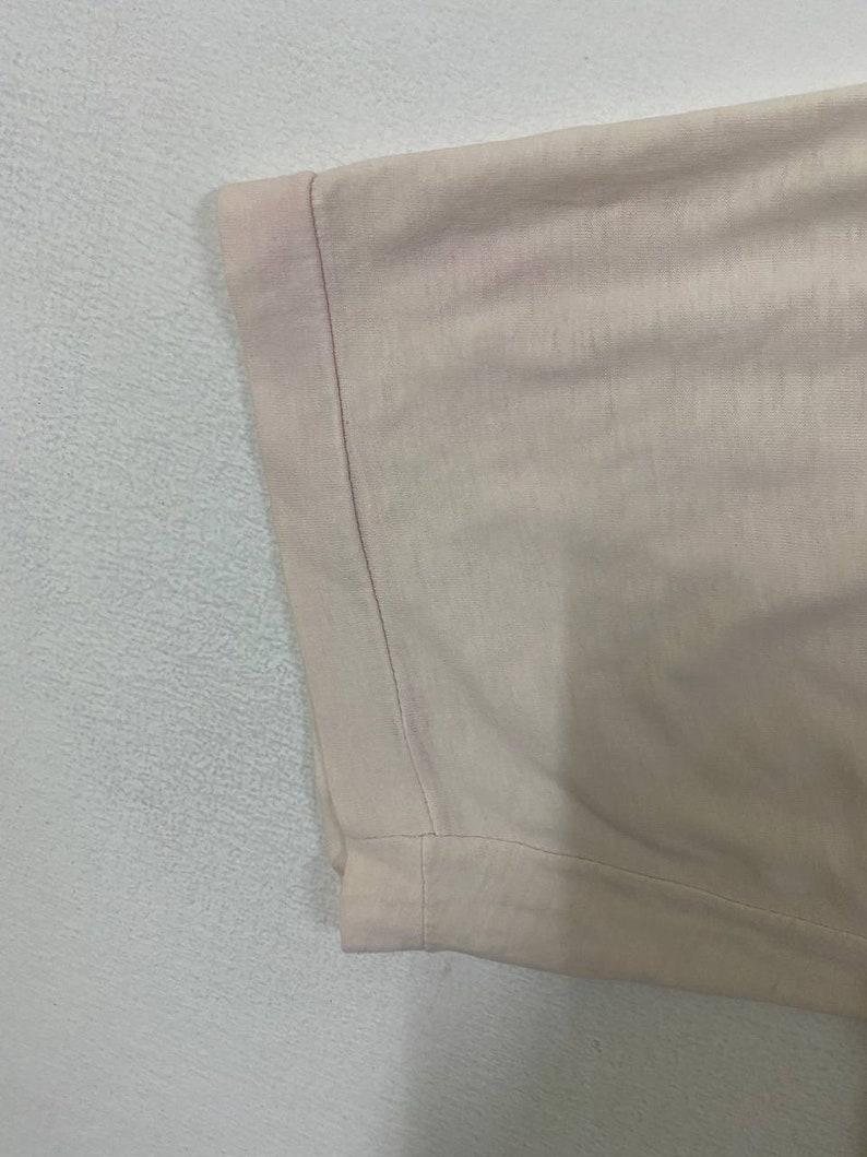 Puede incluir: Primer plano del dobladillo de una camiseta rosa claro. El dobladillo est&aacute; doblado y cosido.