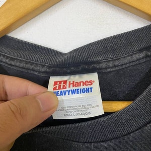 May include: A black Hanes Heavyweight t-shirt tag with white text. The tag says "100% preshrunk cotton", "SA made components assembled in Mexico", "Care on reverse", and "Adult L (42-44)/G/G".