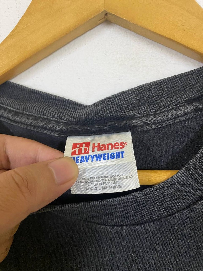 May include: A black Hanes Heavyweight t-shirt tag with white text. The tag says "100% preshrunk cotton", "SA made components assembled in Mexico", "Care on reverse", and "Adult L (42-44)/G/G".