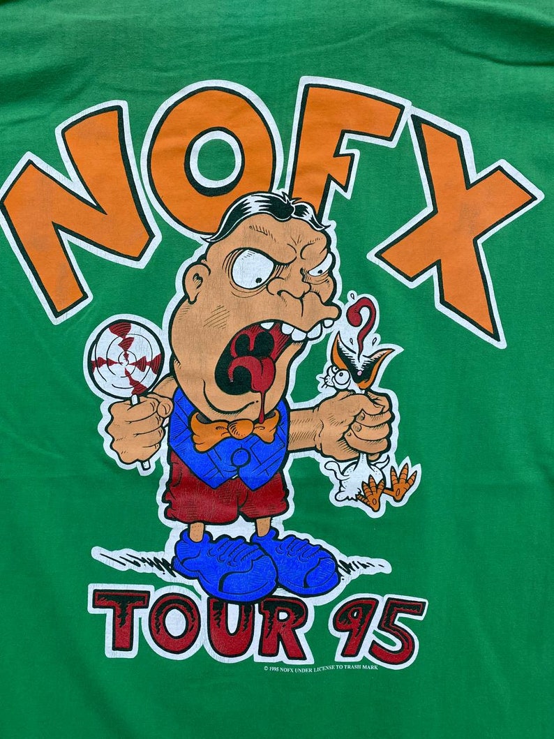 Puede incluir: Camiseta verde con un logotipo "NOFX" naranja y blanco y un personaje de dibujos animados que sostiene una piruleta y un p&aacute;jaro. El texto "TOUR 95" est&aacute; impreso debajo del personaje. El texto de copyright "&copy; 1995 NOFX UNDER LICENSE TO TRASH MARK" est&aacute; impreso en la parte inferior.