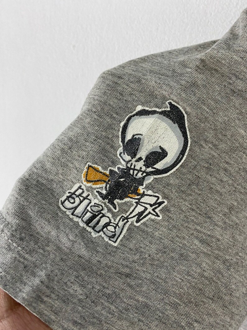 K&ouml;nnte beinhalten: Graues T-Shirt mit einem schwarz-wei&szlig;en Cartoon-Sch&auml;del-Motiv und dem Wort "Blind" auf der Vorderseite.