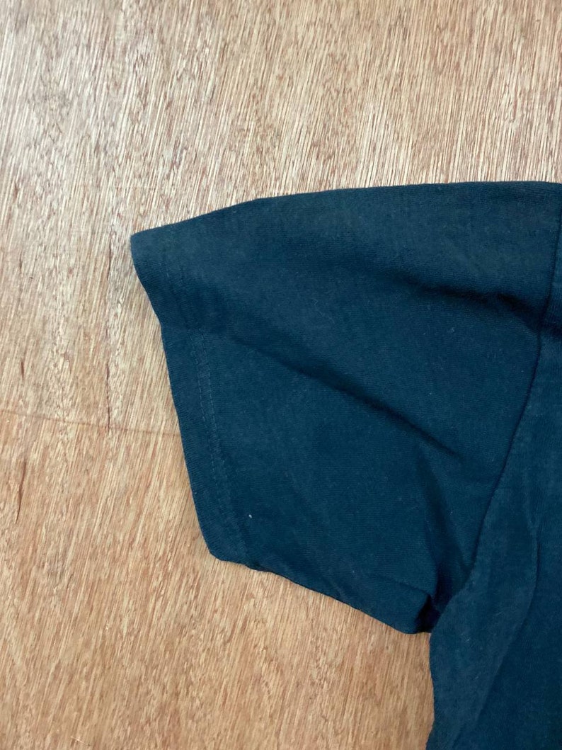 Puede incluir: Primer plano de la manga azul oscuro de una camiseta. La tela es lisa y parece ser de algod&oacute;n.