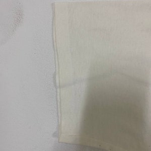 Pu&ograve; includere: Primo piano del bordo inferiore di una maglietta bianca. Il tessuto &egrave; liscio e sembra essere di cotone.