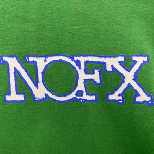 Puede incluir: Una camiseta verde con un logotipo "NOFX" blanco en un contorno azul.