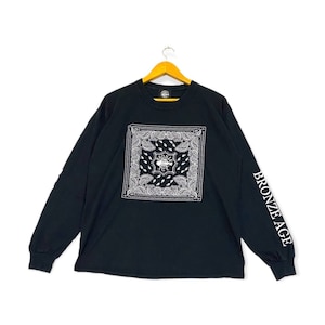 Puede incluir: Camiseta negra de manga larga con un estampado de bandana blanco en la parte delantera y "BRONZE AGE" impreso en la manga derecha.