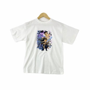 May include: White t-shirt with a graphic print of two anime characters. The characters are in a purple and blue color scheme. The text on the shirt is in Japanese and reads "天 地 創造".
